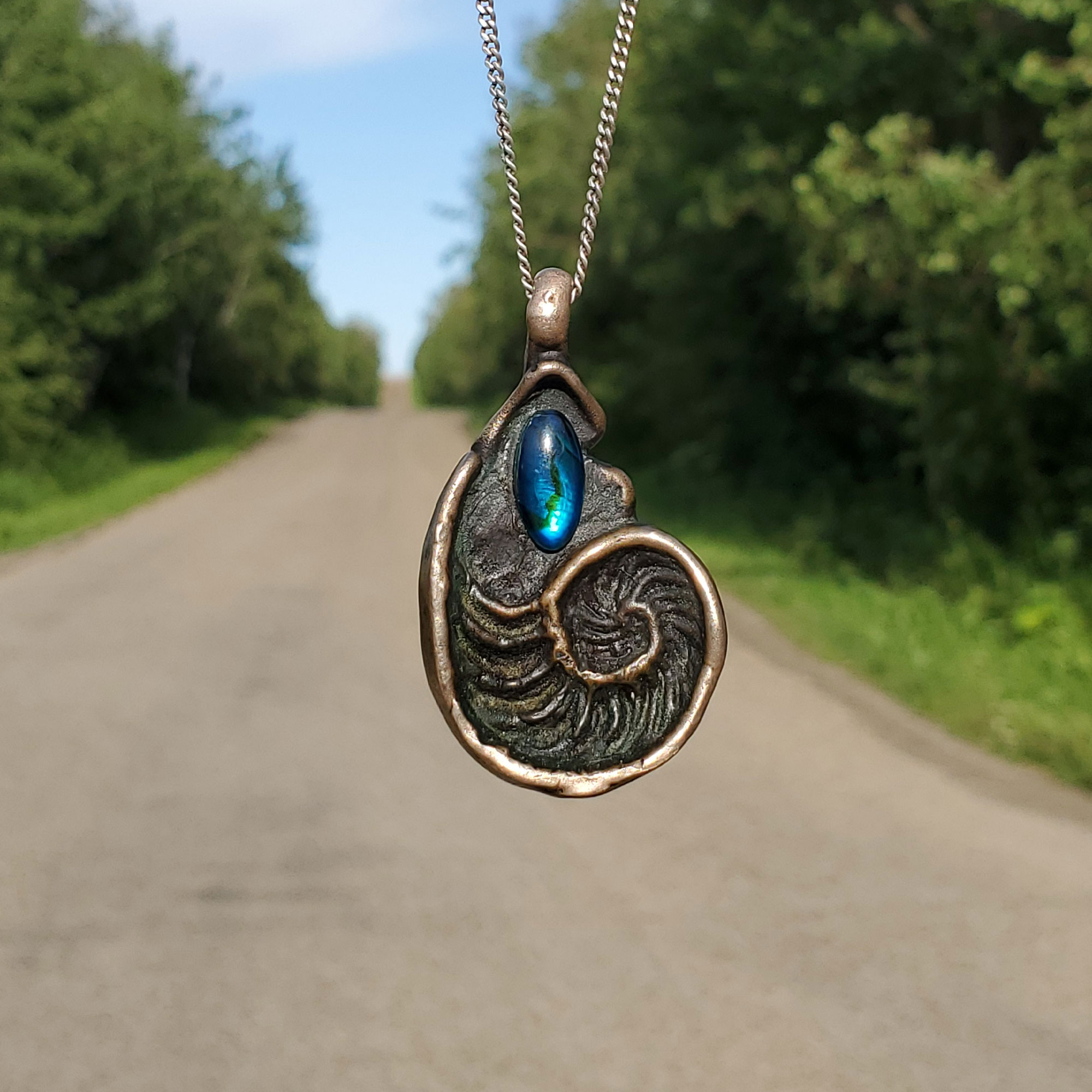 A shell-shaped flat pendant made out of bronze, with an abalone cabochon glued inside of it.